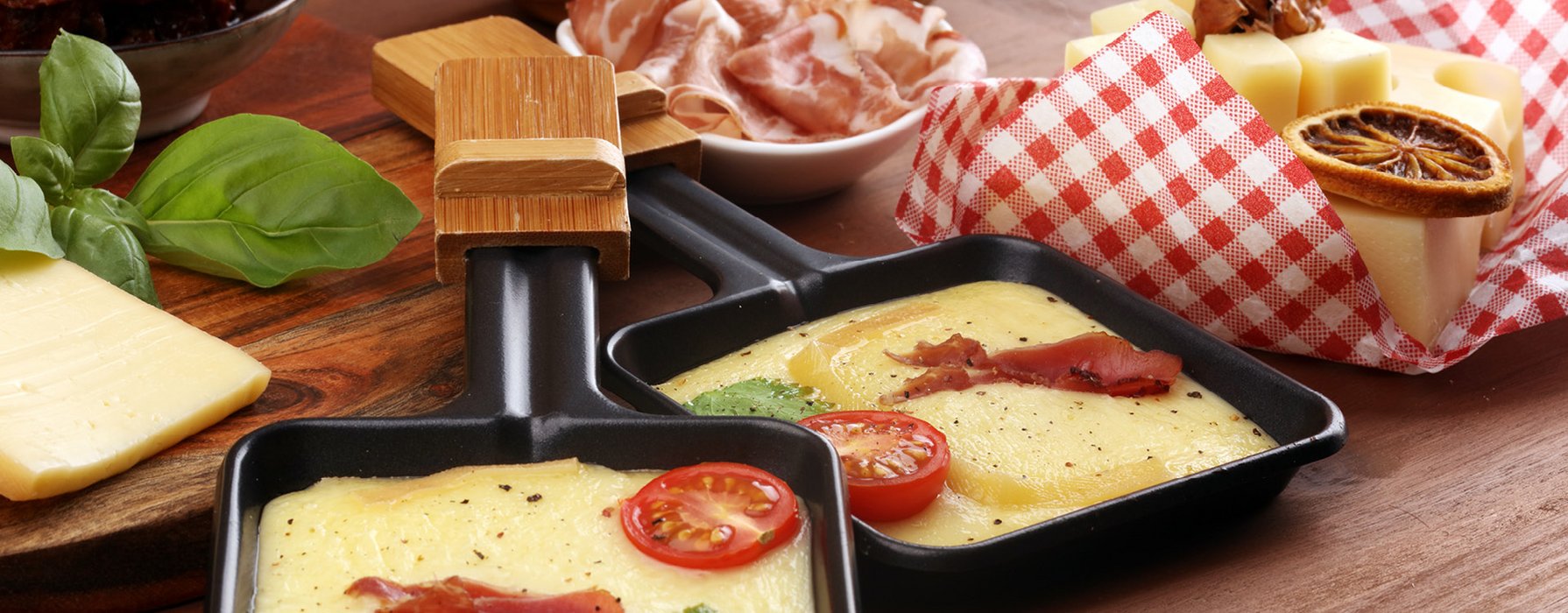 Cooked raclette cheese garnished with meat and tomato in a coated tiny raclette pan