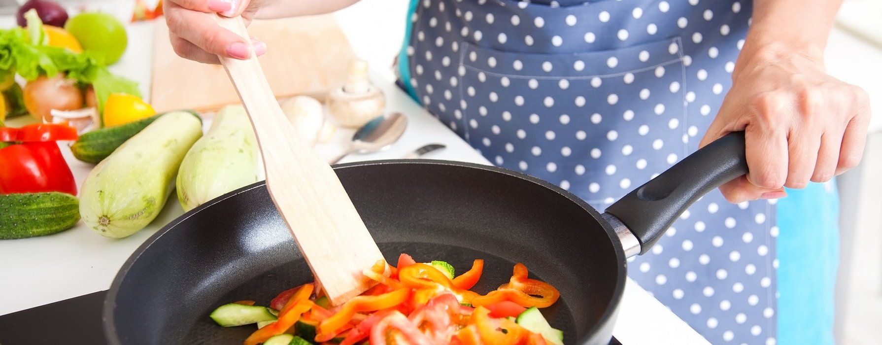 Red pepper and green zucchini are roasted in a black frying pan with a wooden trowel