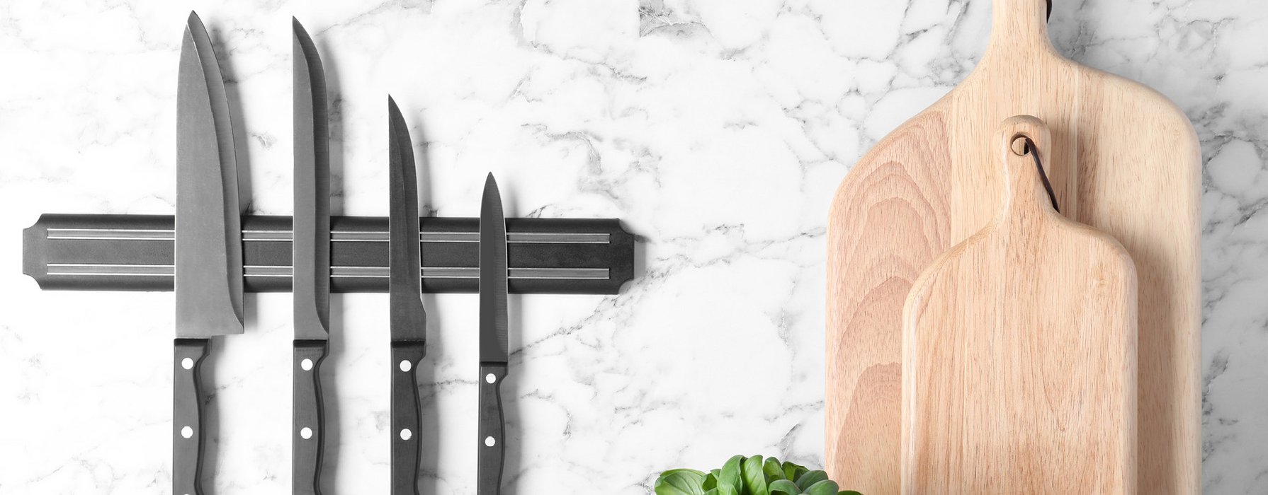 Four carving knives with dark grey blades and black handlesn stick on a magnetic strip on the wall. Next to them are two wooden cutting boards.