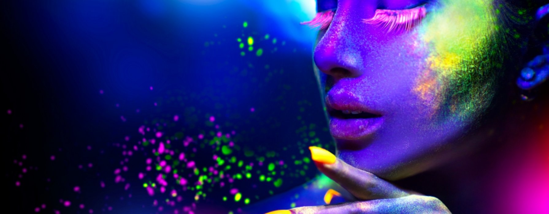 Gesicht einer Frau mit neonfarbigem Makeup vor einem dunkel blauen Hintergrund mit neonfarbigen Highlights. 