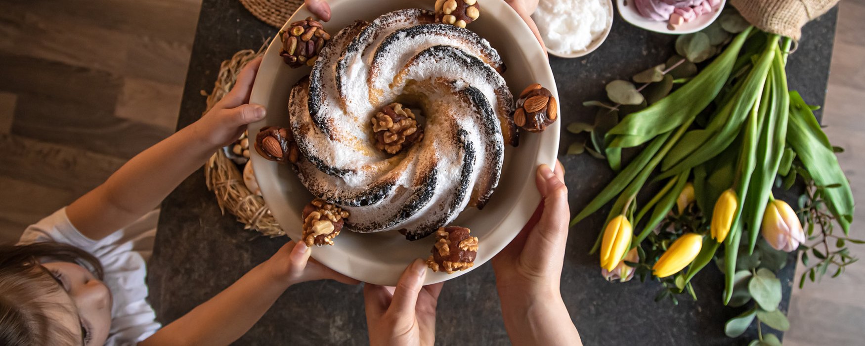 Presentation of a finished baked ring cake in a big bowl. It is garnished with nuts and powdered sugar on top.