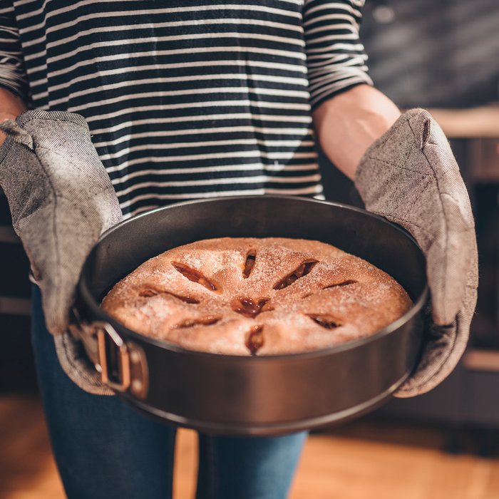 Überbackener Kuchen wird in einer schwarzen, runden beschichteten Springform zum Tisch getragen