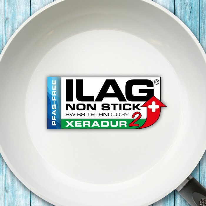 Weisse Innenseite einer Bratpfanne - mittig das ILAG Logo mit grün unterlegtem Xeradur 2 Schriftzug und links zusätzlicher Beschriftung "PFAS-FREE" in blau