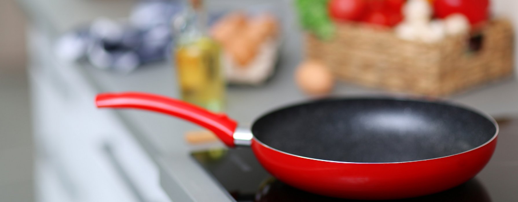 Pan with a red handle, red coating on the outside and black coating on the inside is standing on a induction cooker.