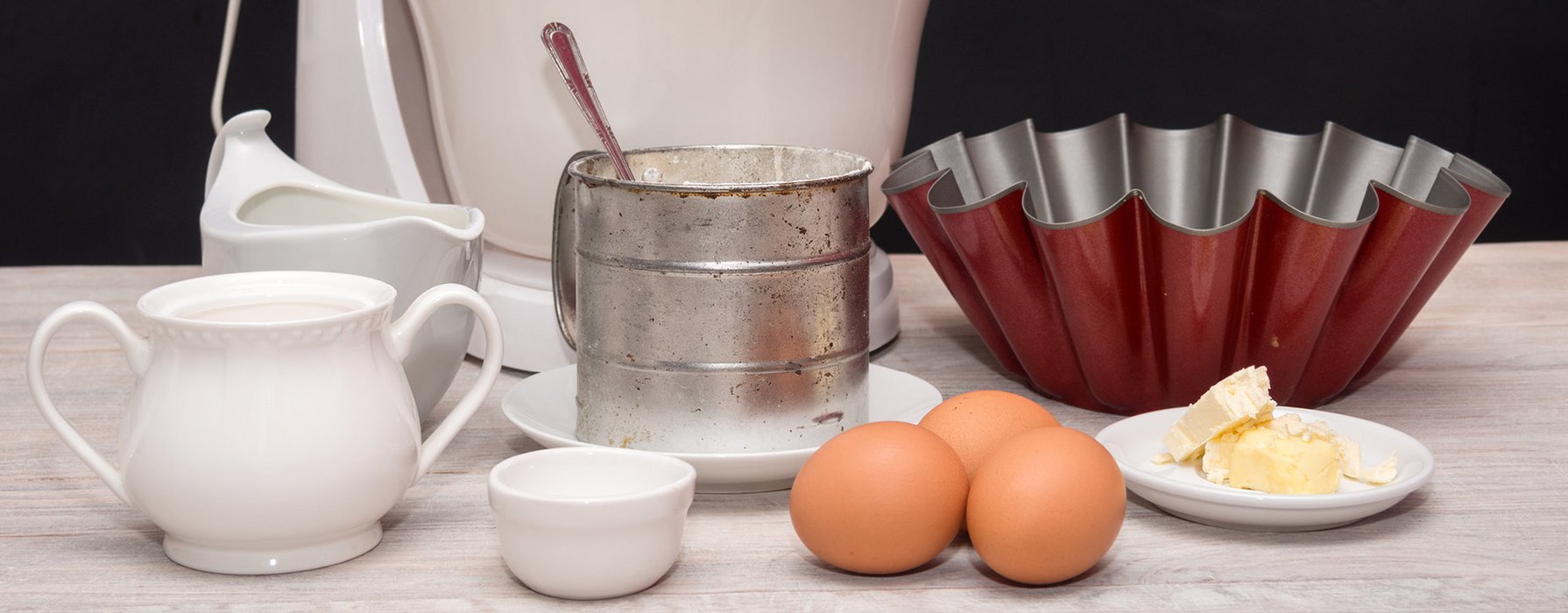 A cake tin with high and wavy edge is standing on the table with some other baking ingredients.