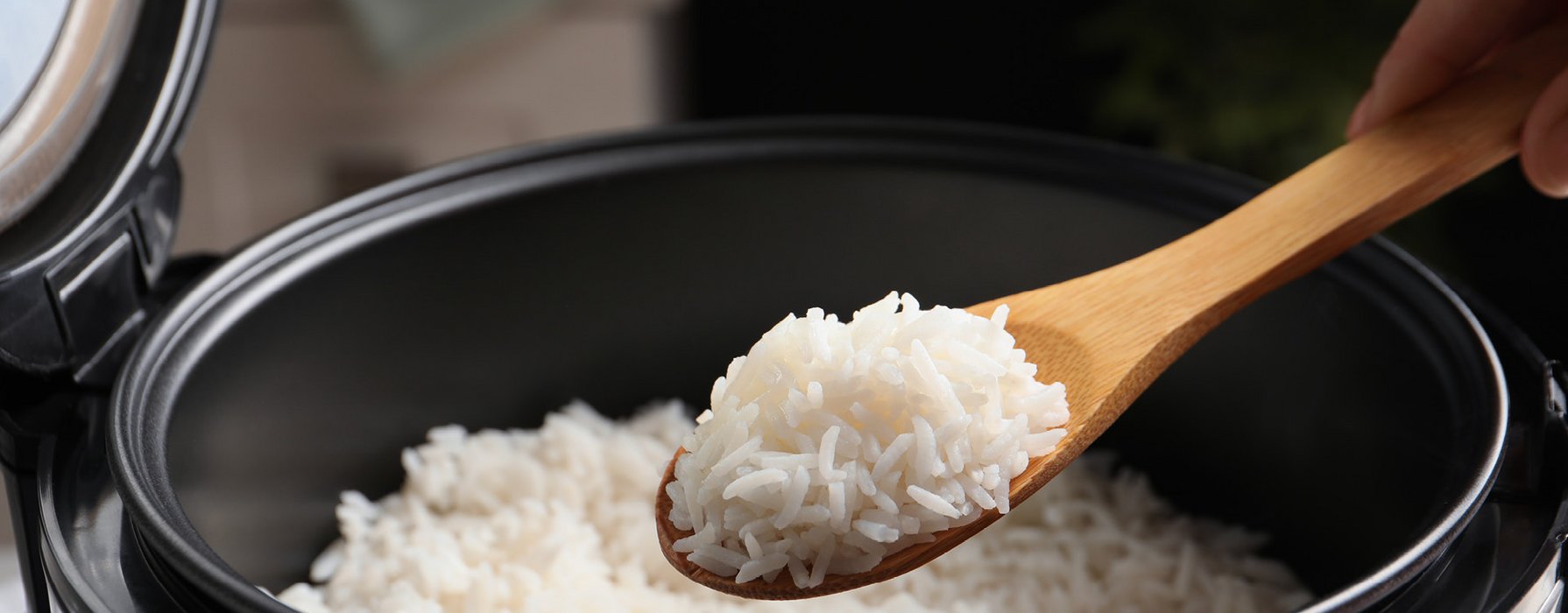 From the black coated inside of a rice cooker some cooked rice is served with a wooden spoon
