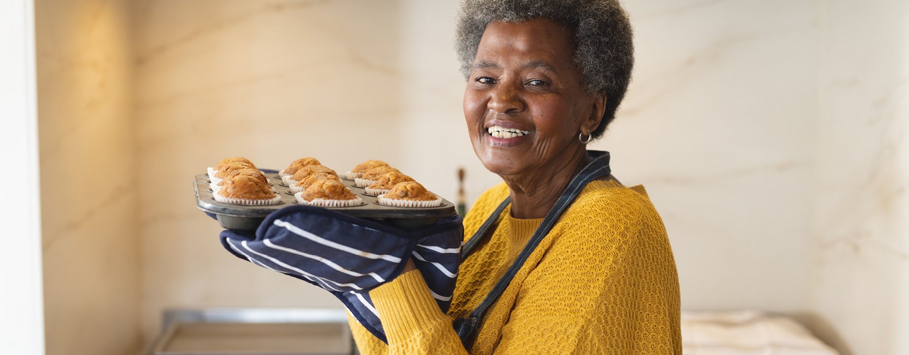 Ältere Dame hält freudig eine Muffinform mit gebackenen Kuchen in den Händen