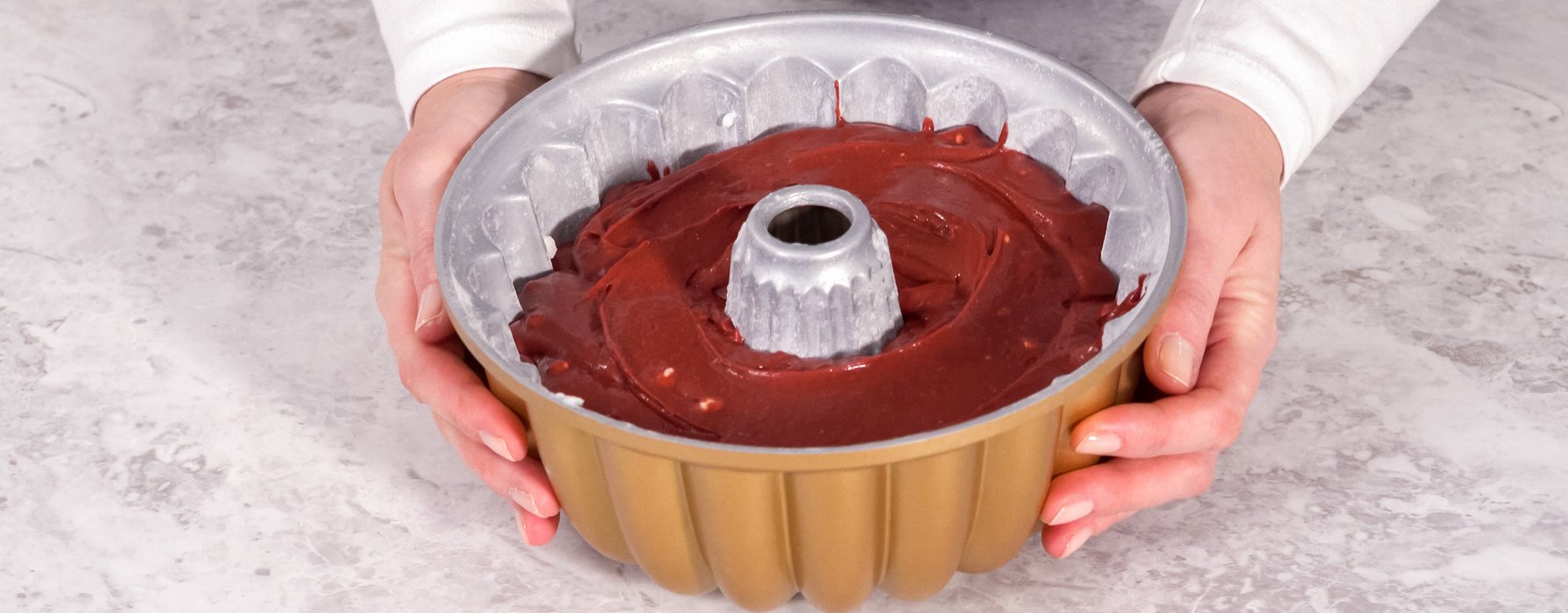 Bundt cake pan with golden outside coating and bright chocolate dough in it is placing on the table