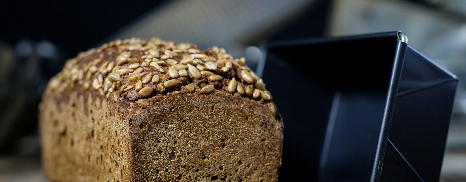 Ein gebackenes Brot steht neben einer schwarzen Kastenform