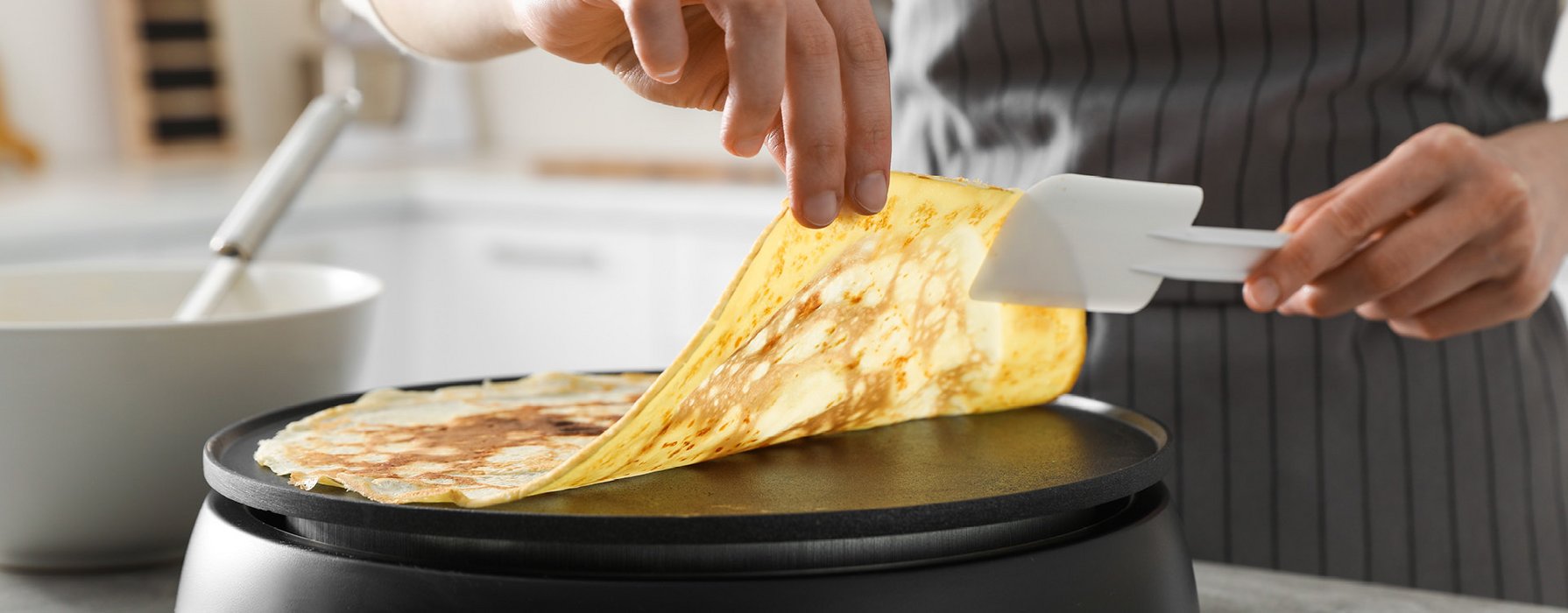 A grilled crepe is lifted up from the grill plate with help of a plastic trowel