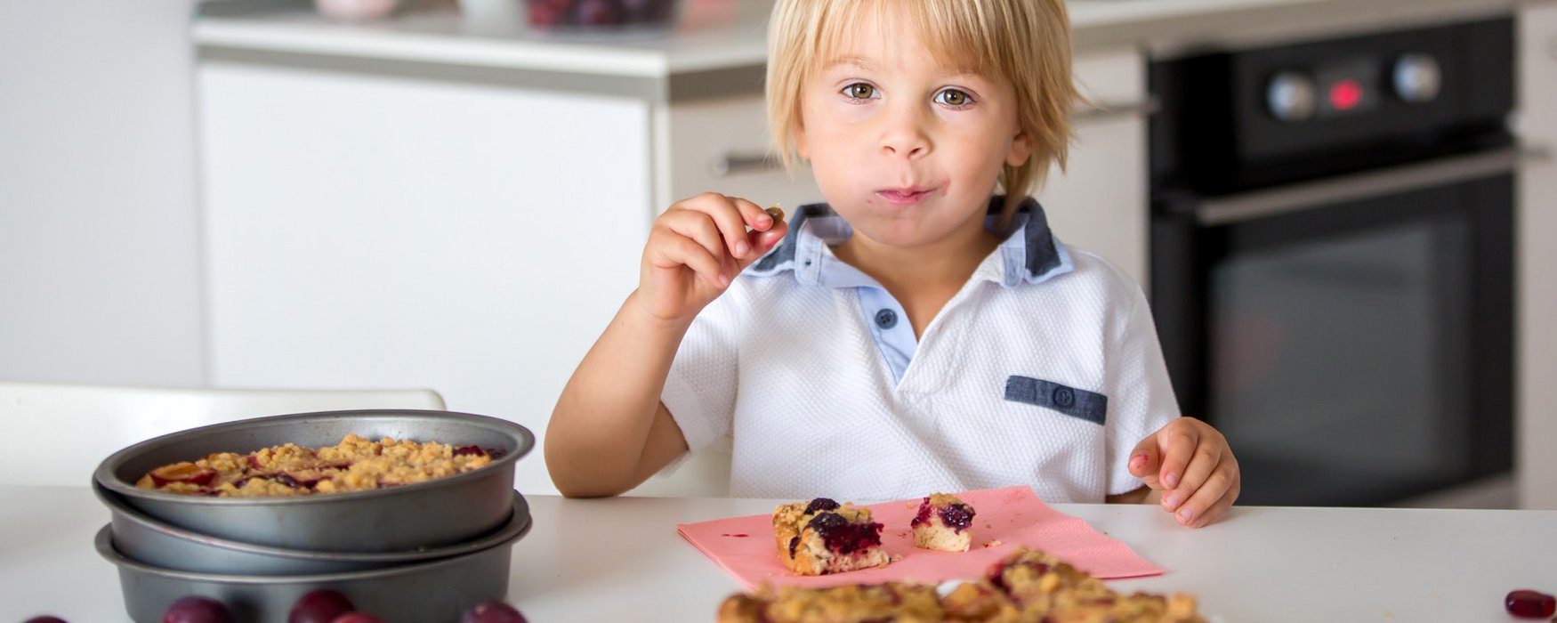 Kleiner Junge nascht Mürbekuchen mit Beeren aus einer Kuchenform
