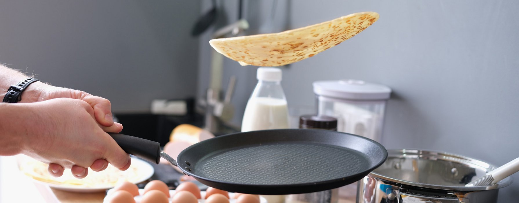 Out of a flat, black omelette pan a fryed pancake is flipped in the air