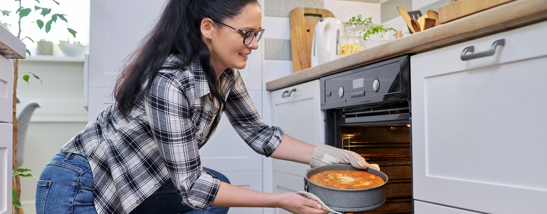 Young woman is taking a filled cake pan with grey speckled outside out of the oven