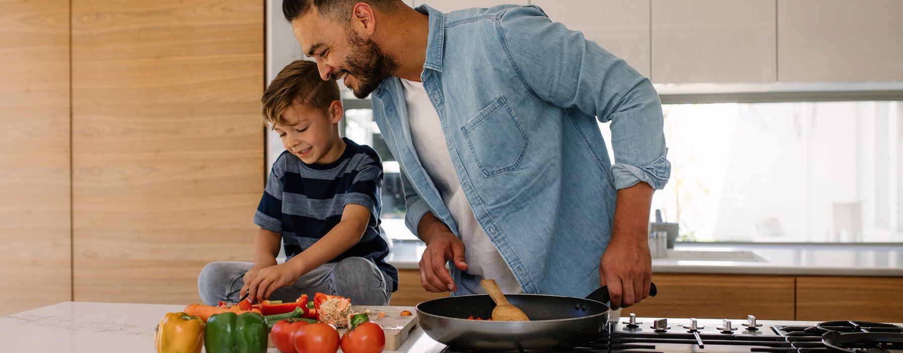 Little boy cuts some vegetables which his father wants to cook in a frying pan