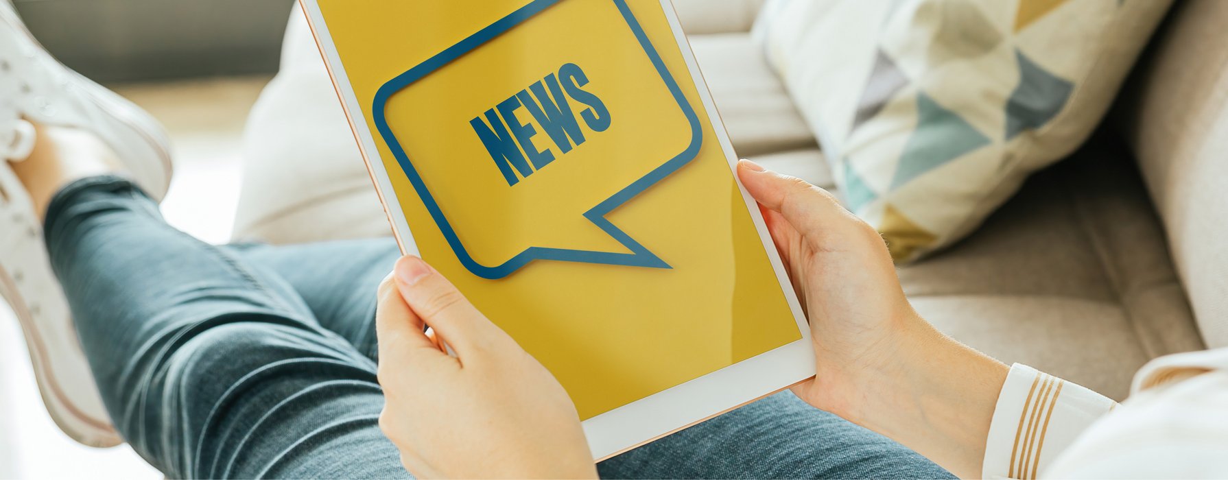 Dame mit hochgelagerten Beinen auf dem Sofa mit einem Plakat mit Aufschrift News in der Hand
