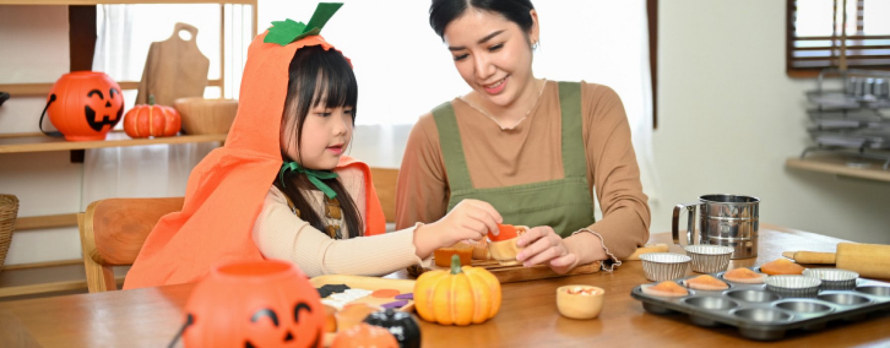 Mother and child baking Halloween treats, surrounded by pumpkins and baking utensils at the table.