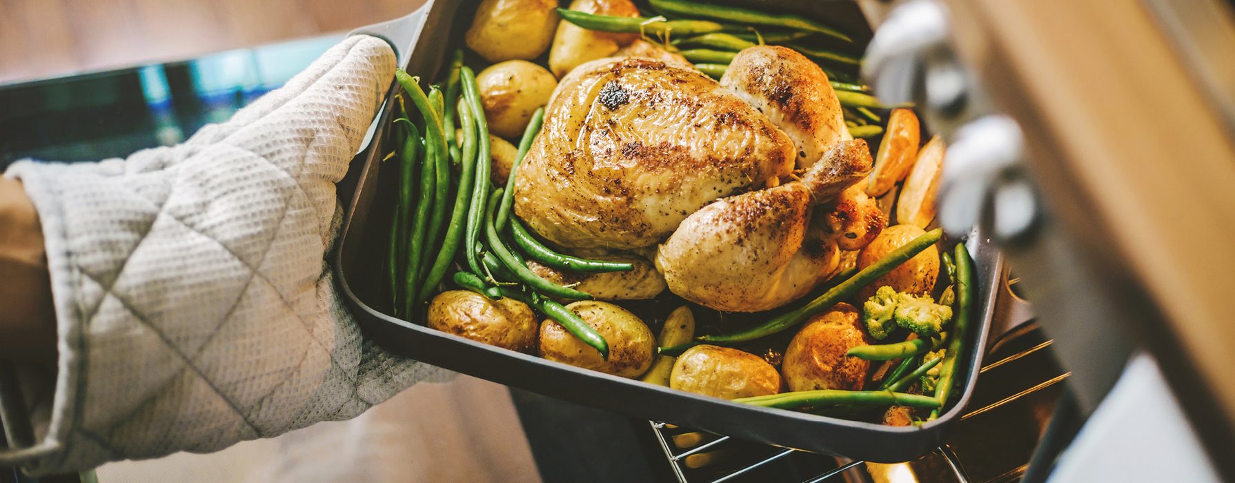 Roasted chicken in a casserole dish garnished with potatoes and beans is taken out of the oven