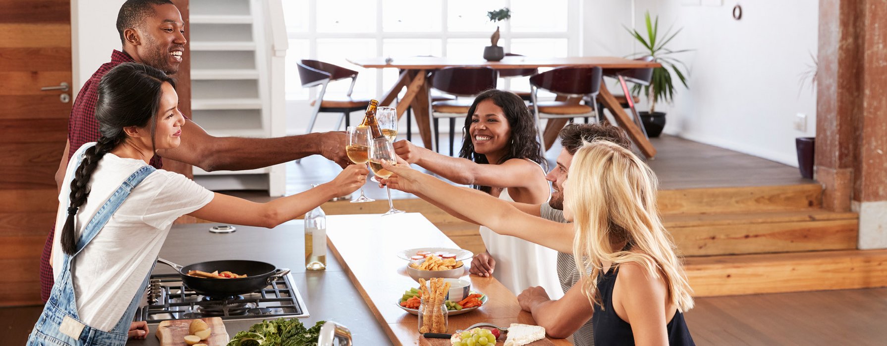 Fünf Erwachsene stossen mit Weingläser und Bier am Tisch an 