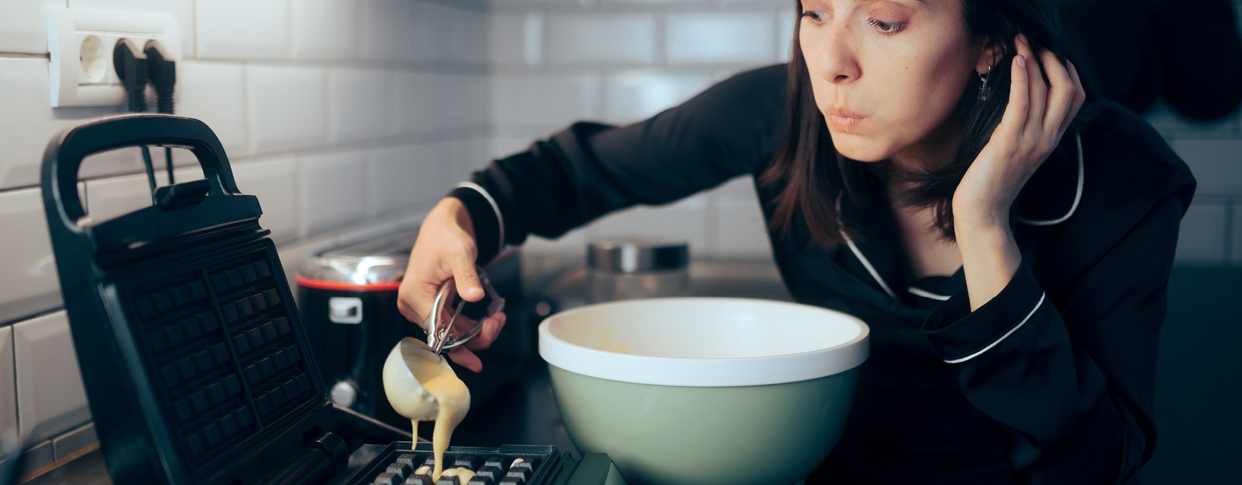 Junge Dame füllt mit einem Eisportionierer Flüssigteig in ein schwarz beschichtetes Belgisches Waffeleisen